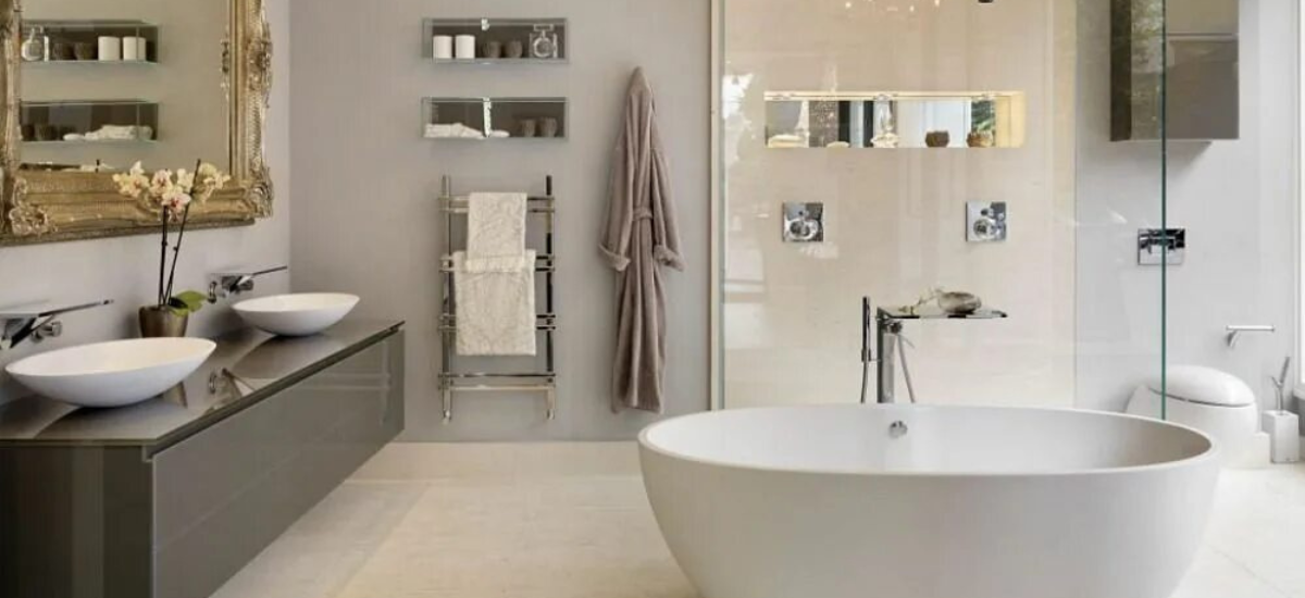 Элегантная ванная комната в светлых тонах с отдельностоящей ванной, двойной раковиной на подвесной тумбе, полотенцесушителем и декоративными аксессуарами.